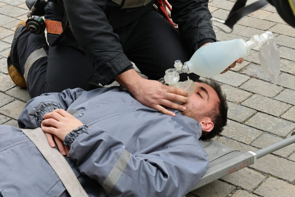 Firefighter providing oxygen mask to injured person during rescue operation outdoors.