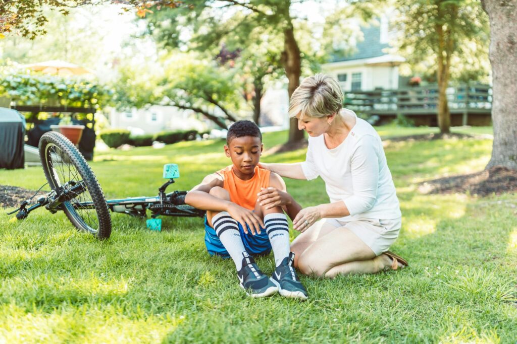 A caring mother tends to her son after a small bicycle accident in a sunny park.