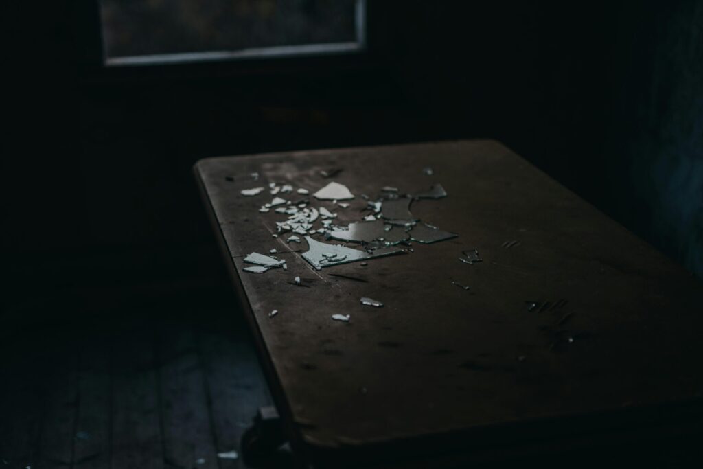 A moody shot of broken glass pieces scattered on an old wooden table in a dimly lit room.